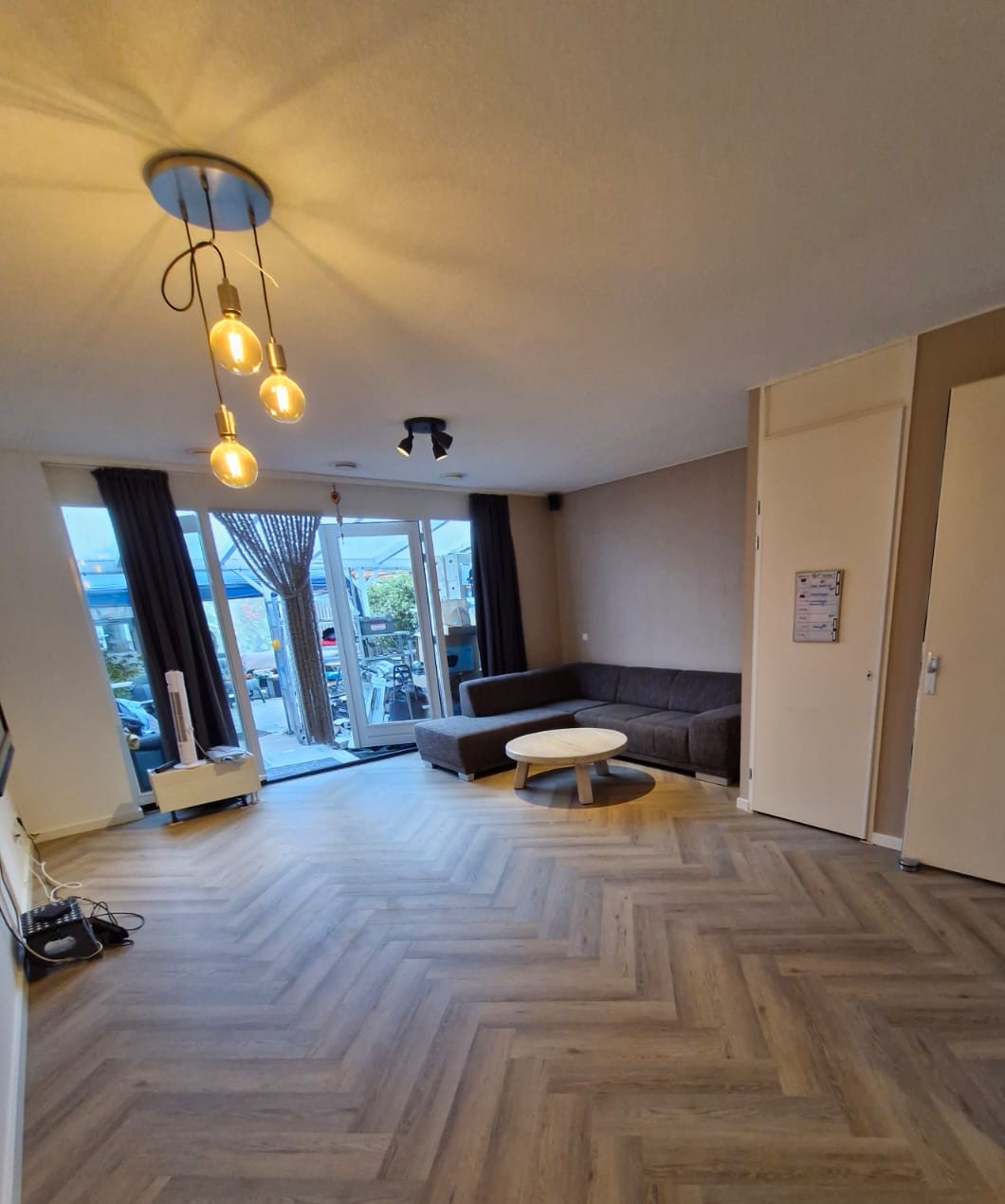 Woonkamer met een grijsbruine PVC visgraatvloer, hanglampen en een hoekbank