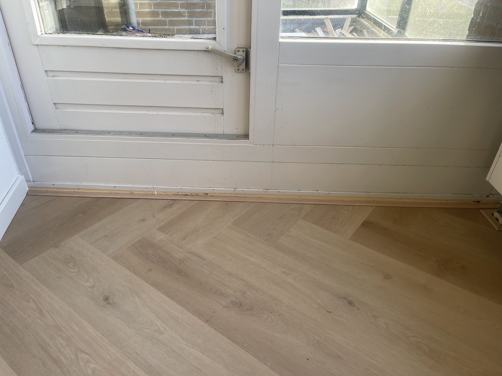 Lichte eiken visgraatvloer die aansluit op een witte balkondeur