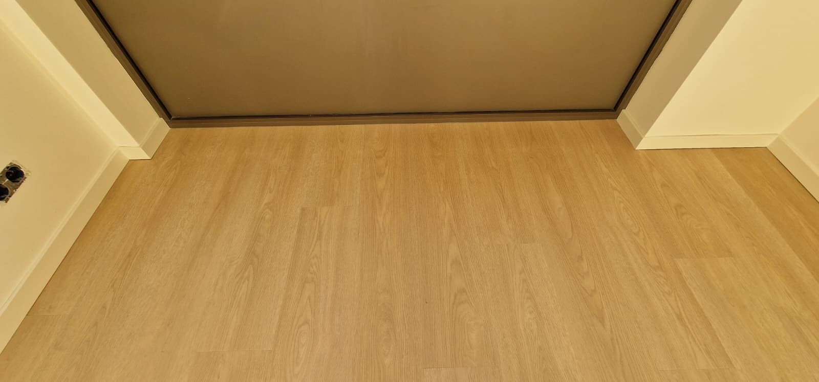 Lichte eiken PVC-vloer in een lege kamer met witte plinten